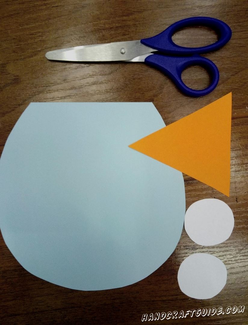 To start, we need to cut out a blue paper circle with one cropped side, an orange triangle and two white small circles
