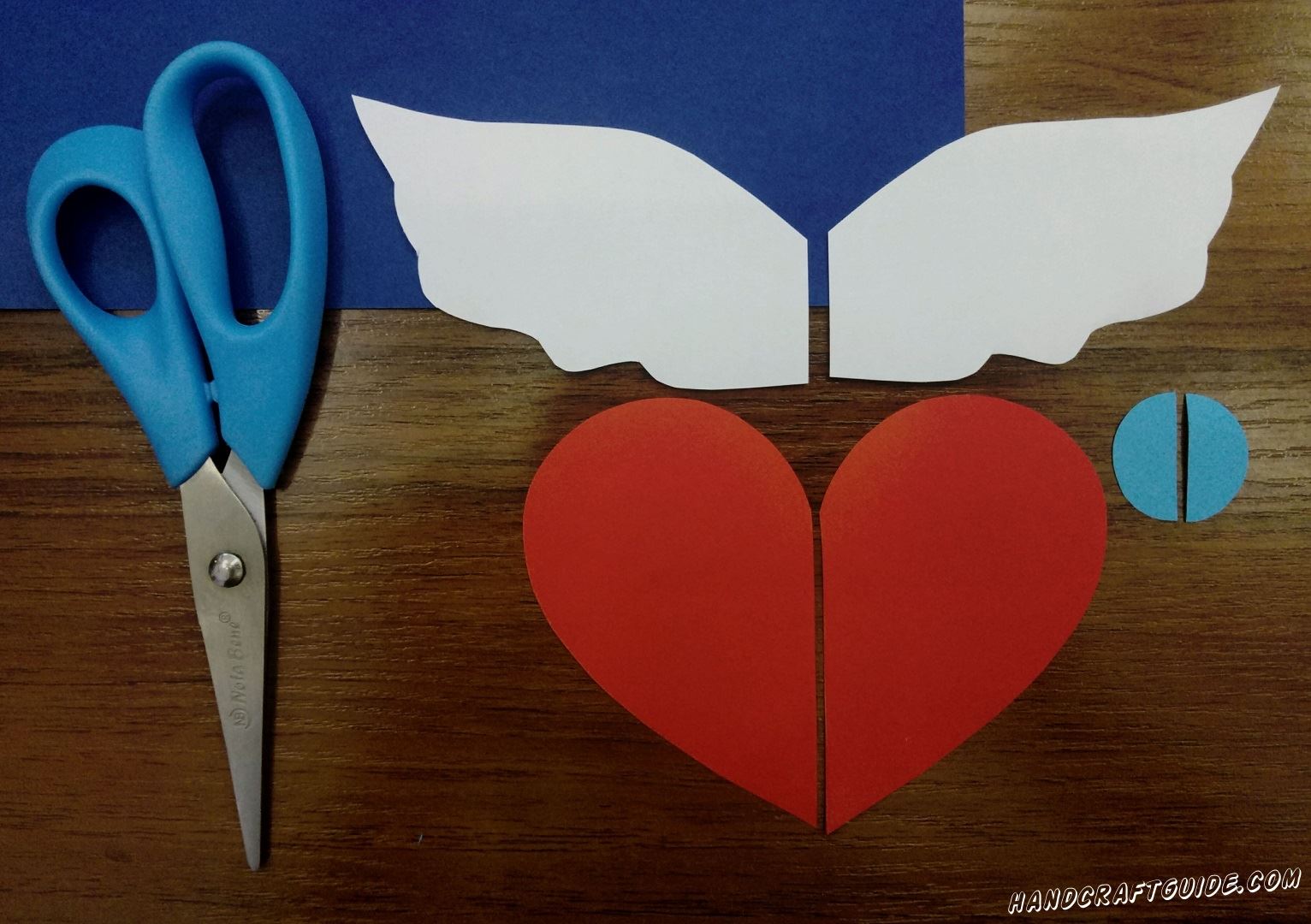 First cut out a large red heart and cut it in half. Then cut the wings out of white paper and also cut out a small blue circle and cut in half. 