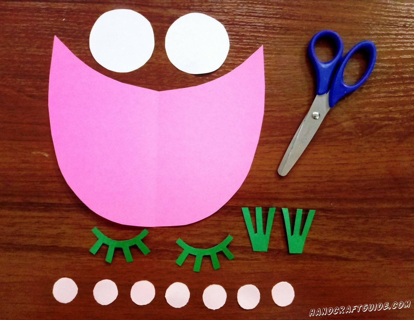 Take pink paper and scissors. Cut out a detail which looks like a boat or a wide smile :) Next take white paper and cut out 2 middle size circles and 7 small circles. Now choose green paper. Cut out eyeslashes and 2 details like crowns. Don't forget to cut a small orange rectangle. You can see how we did it in the photo :) Well done, let's continue... 