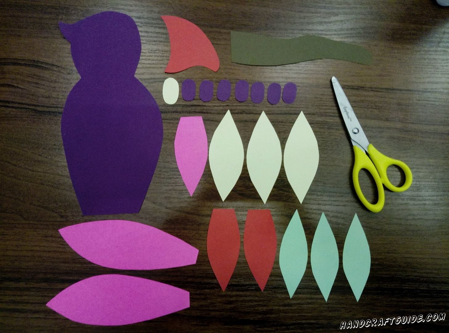 Let's begin with the preparation of all needed deatails. Take purple paper and cut out a figure like an 8 but without holes. Next cut out 7 small ovals from the same paper. Cut out white oval of the same size. Now take purple or pink paper and cut out 2 details, which resemble bunny's ears, and one detail like a tree leaf with a cut edge. Cut out 2 the same "cut" leafs from pink paper. Cut out a detail, like a shark fin, from red paper. Cut 3 petals out of yellow and turquoise paper. And, finally, a brown w