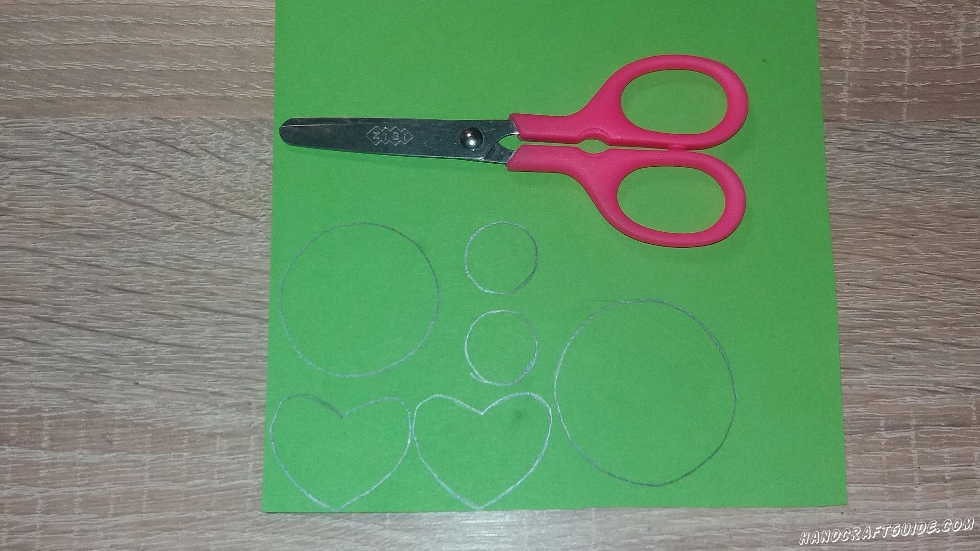 Для начала берем в руки бумагу зеленого цвета и вырезаем все необходимые нам детальки: 2 сердечка, 2 одинаковых маленьких кружка, 1 большой круг и 1 круг немного меньший чем большой