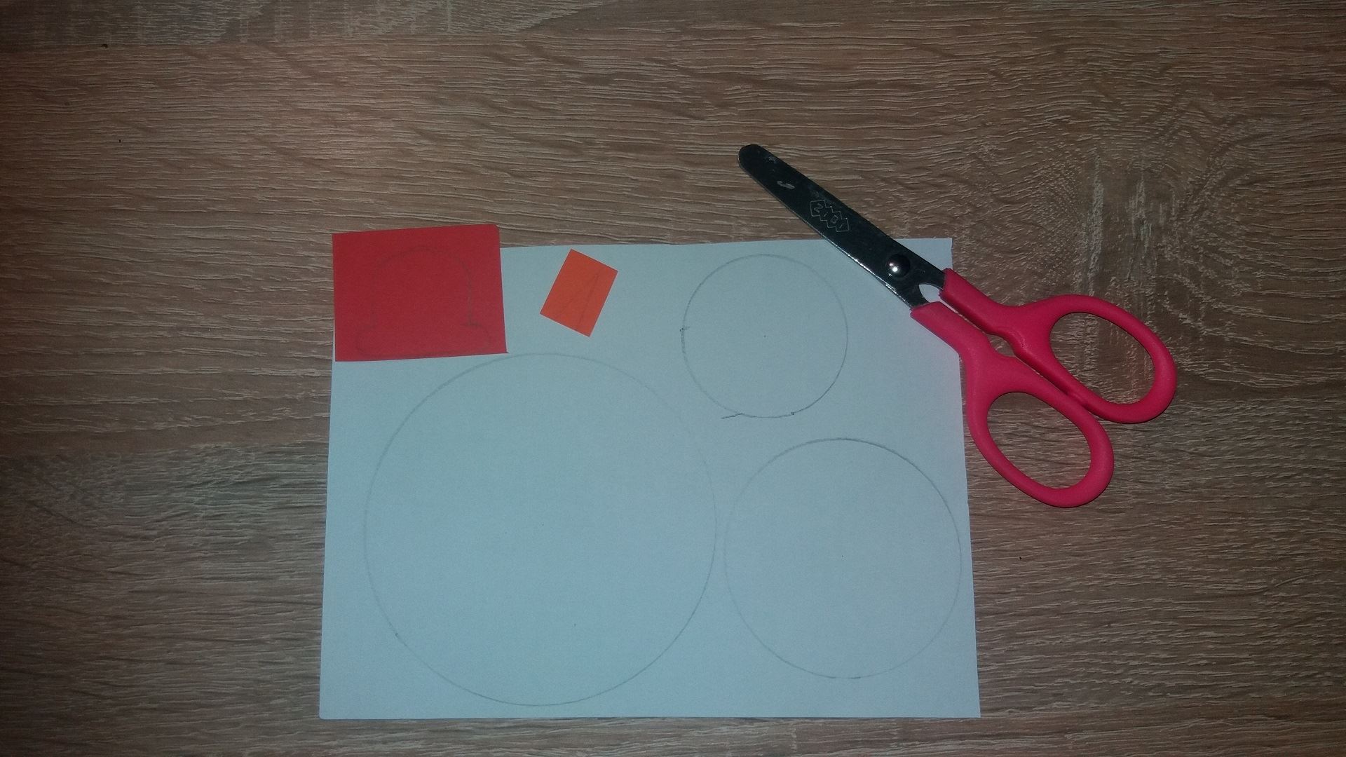 Сначала мы нарисуем 3 ровных круга на белом листе бумаги: большой, средний и маленький. Затем мы рисуем небольшую шляпку на красной бумаге и маленький треугольник на оранжевой бумаге. Вырезаем, что нарисовали 