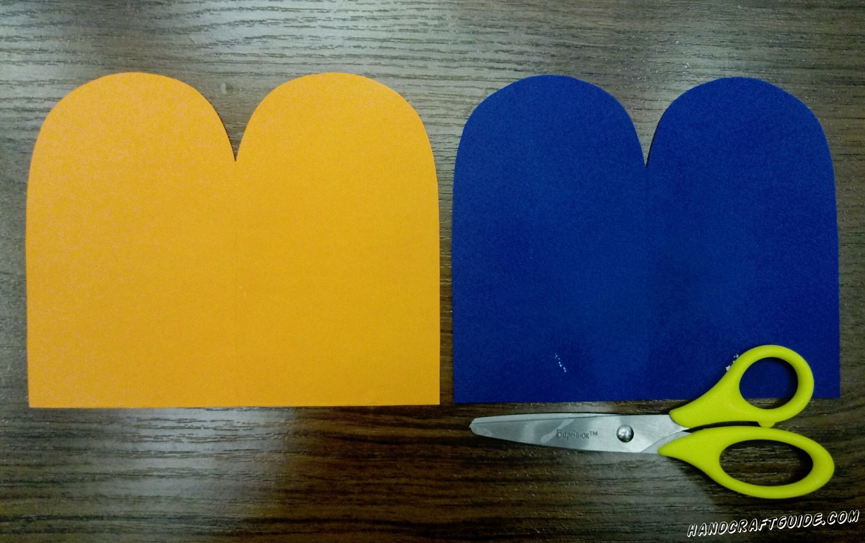Берем в руки оранжевую и синюю бумагу. Вырезаем по одному одинаковому прямоугольнику каждого цвета. Затем прикладываем два цвета друг к другу и рисуем два бугорка с одной стороны. Обрезаем лишнее и у нас выходит две одинаковые фигурки разного цвета.