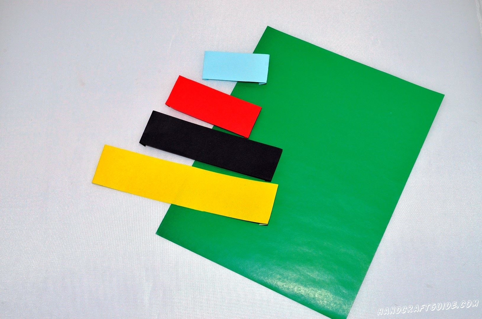 Берем цветную бумагу и вырезаем 4 полоски одинаковой ширины, но не длинны: самая длинная – желтая, потом - черная,  красная и самая короткая – голубая.