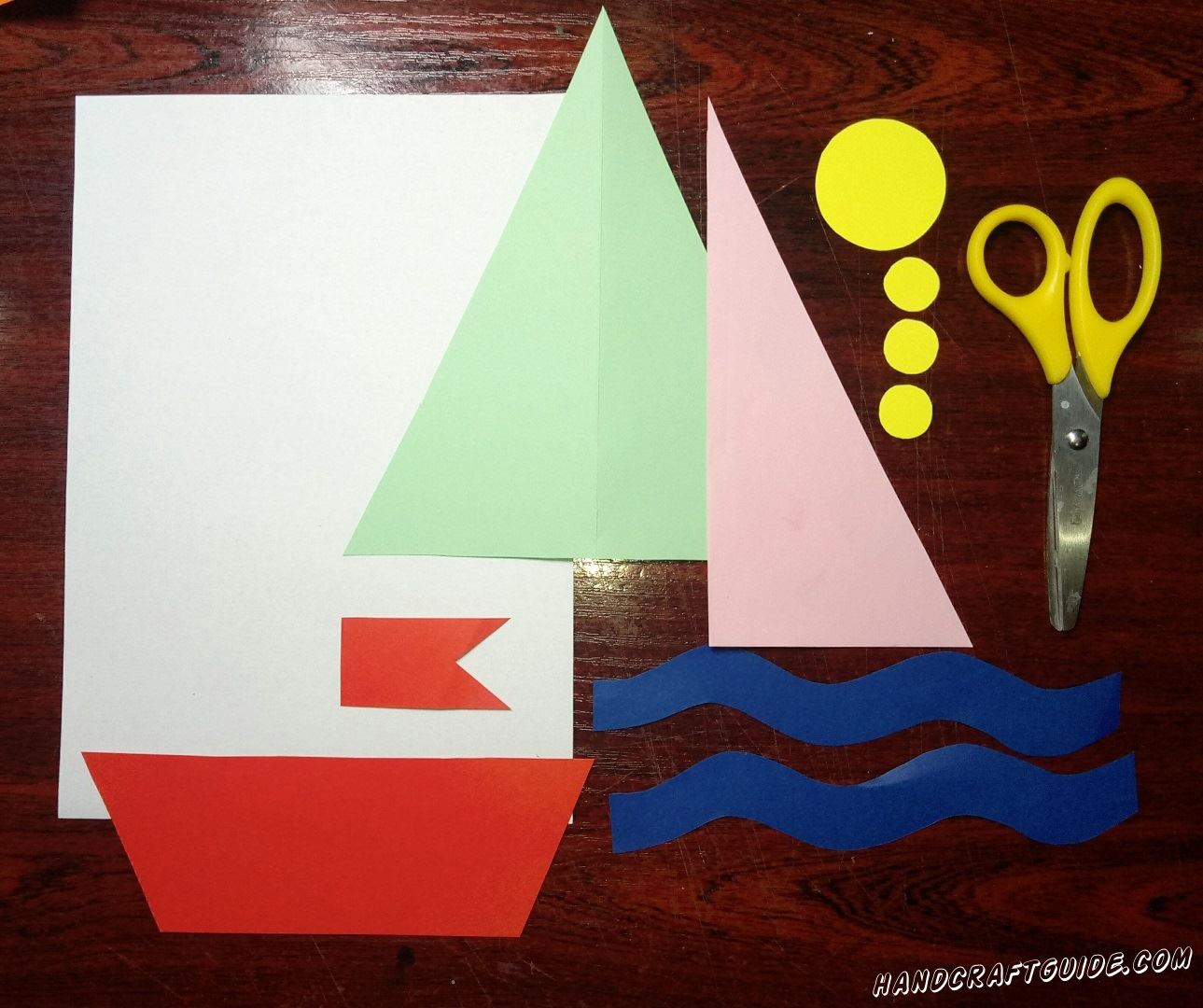 Вырезаем из бумаги все необходимые нам детали: красную основу корабля и флажок, две синие волны, розовый и светло-зелёный паруса, один большой и три маленьких кружочка желтого цвета.